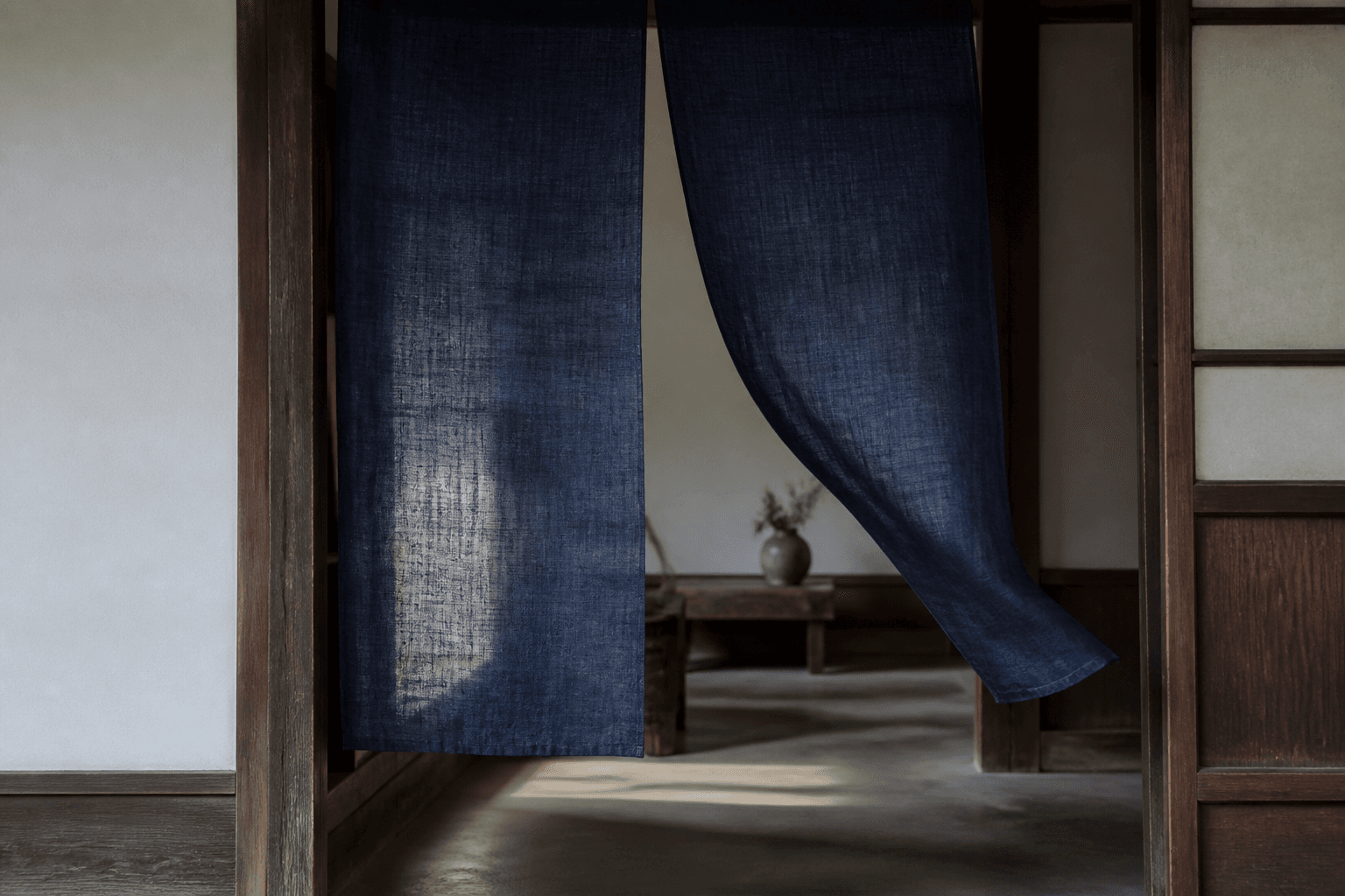 An indigo noren moving gently in a wooden Japanese doorway