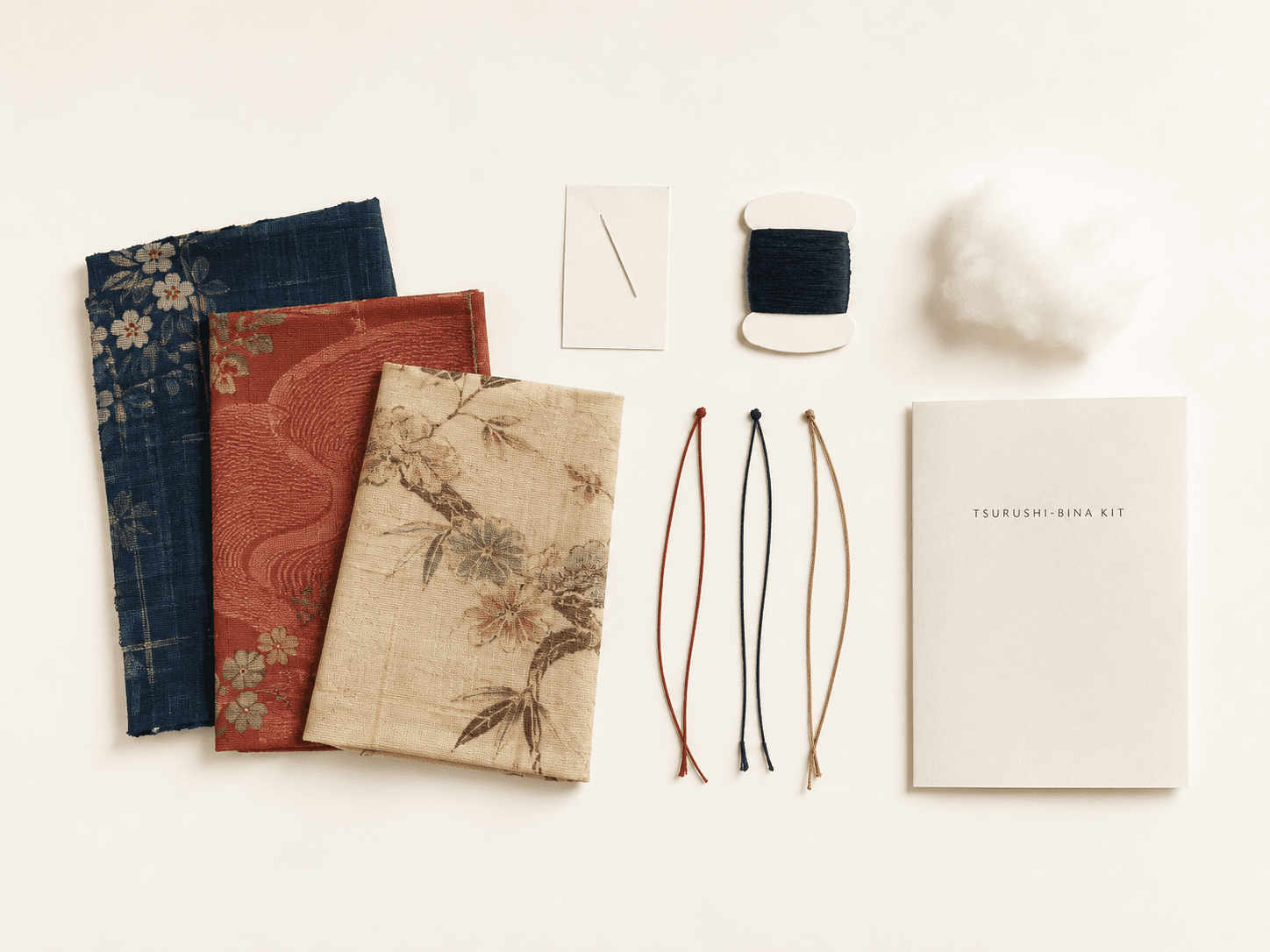 Example arrangement of kimono cloth, a needle, thread, soft filling, hanging cords, and an English instruction guide included in the Tsurushi-bina kit